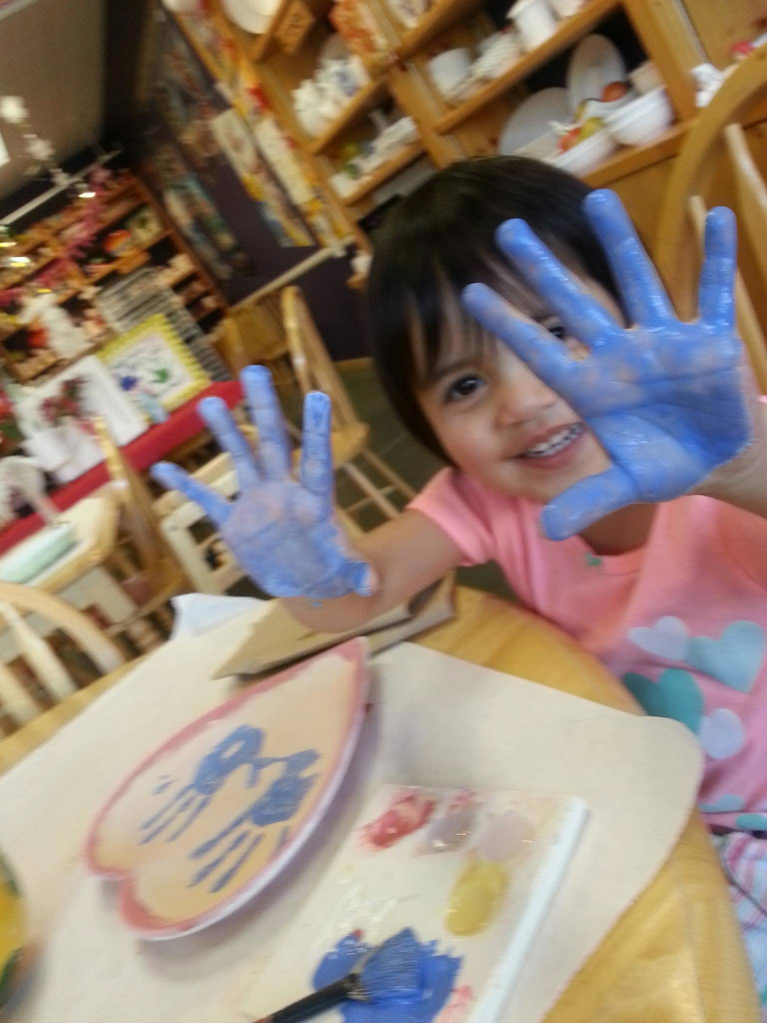 young Scarlette showing off blue painted hands at a pottery studio