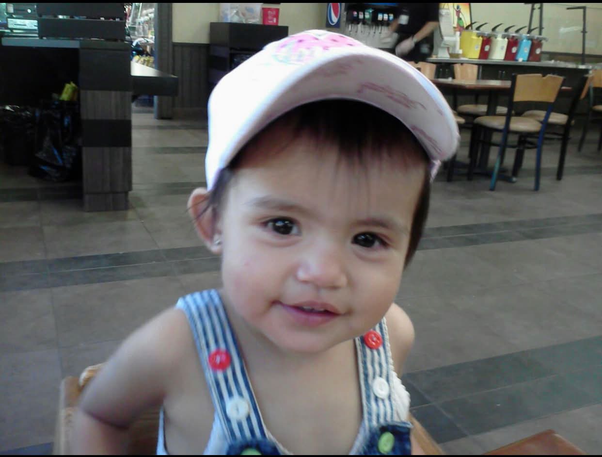 baby Scarlette in a pink cap and denim overalls